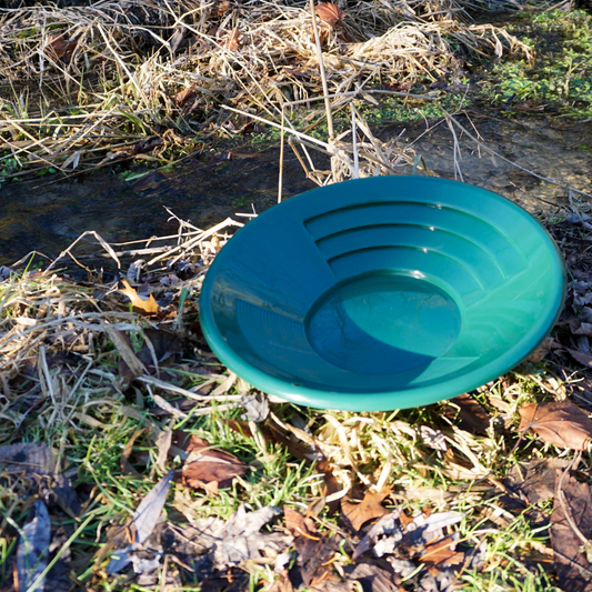 NubuClo gold prospecting pan displayed outdoors in natural terrain.

